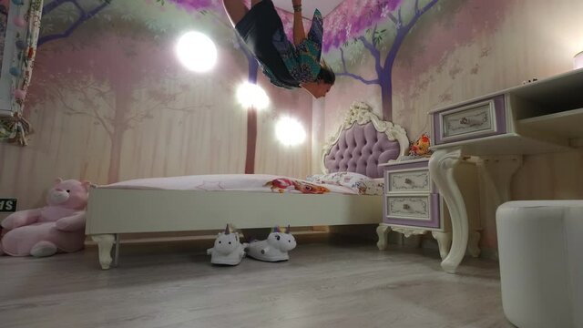 Fantastical shot of girl floating above bed in a white and pink bedroom
