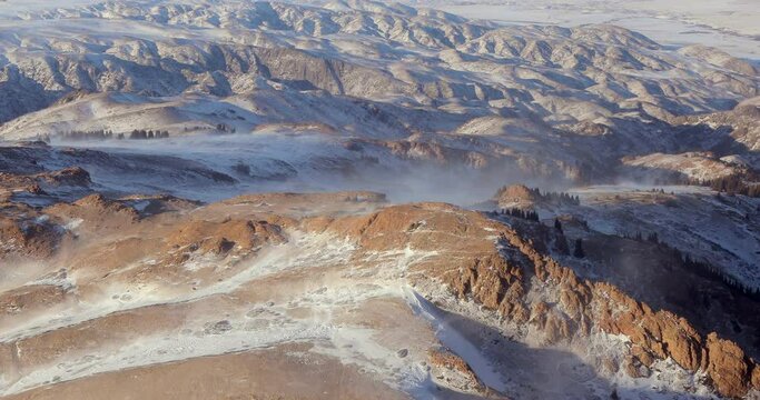 Aerial view of rocky mountain ranges in winter. Mountains in the snow with ridges in a beautiful landscape in Kazakhstan. Snowstorm sweeps snow on mountain peaks.