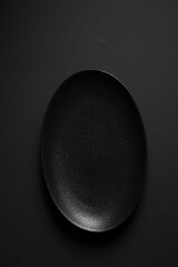 Empty black plate with a copy space for food on a dark grey background. Mockup. Top view, vertical orientation.