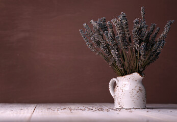 Bouquet of dried lavender flowers in a clay white pitcher with a copy space on a brown background.