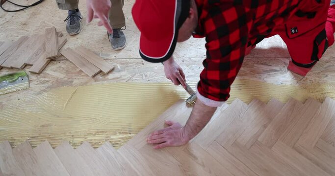 Carpenter worker installing wooden floor, parquet in an apartment during renovation. Worker installing wood parquet. Construction in a renovated room installation of parquet