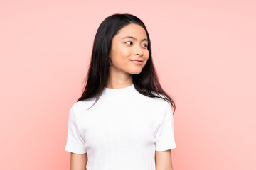 Fototapeta premium Teenager Chinese woman isolated on pink background looking to the side and smiling
