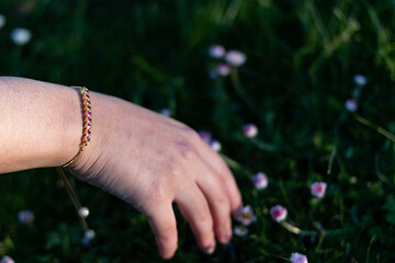 hand with jewelry and flowers in the grass
