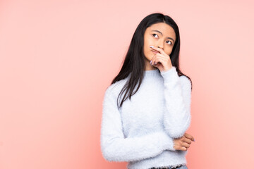 Teenager Chinese woman isolated on pink background having doubts and with confuse face expression