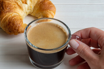 hand holding cup of black coffee croissant