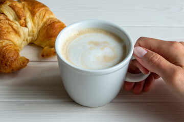 hand holding cup of cappuccino croissant white background