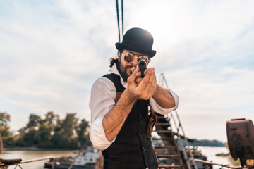 Obraz premium Steampunk. A hero on a river barge surrounded by steel mechanisms. A man with a weapon.