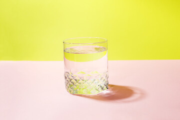 A glass of pure refreshing clear water on a colored pink and yellow background. The concept of daily water consumption for body health