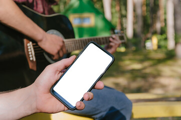 Mock up of a smartphone in front of a man playing the guitar. Against the background of the forest and houses in nature.