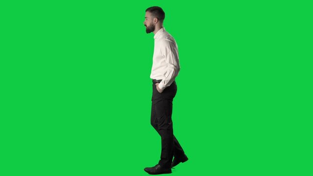 Polite confident business man walking and looking at camera greeting with head nodding. Full body on green screen chroma key background.