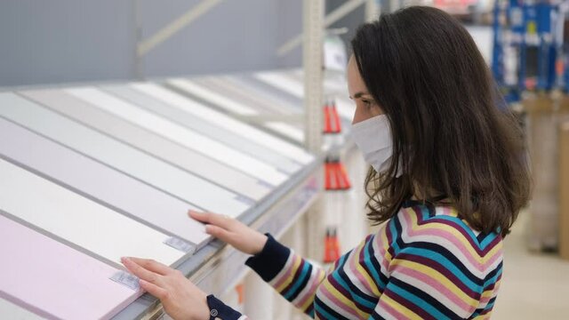 Young Woman in Safety Mask Choosing New Wallpapers for Home at Store. Shopping, Renovation and Redecoration Concept