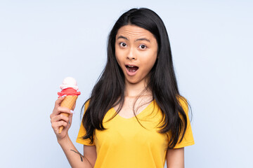 Teenager Asian girl with a cornet ice cream isolated on blue background with surprise and shocked facial expression
