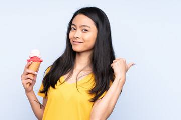 Teenager Asian girl with a cornet ice cream isolated on blue background pointing to the side to present a product