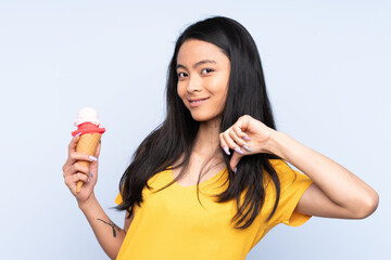 Teenager Asian girl with a cornet ice cream isolated on blue background proud and self-satisfied