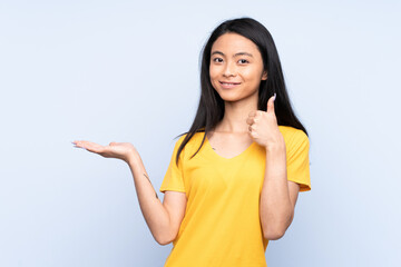 Teenager Chinese woman isolated on blue background holding copyspace imaginary on the palm to...
