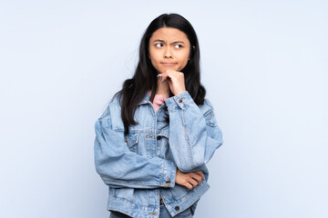 Teenager Chinese woman isolated on blue background having doubts and thinking