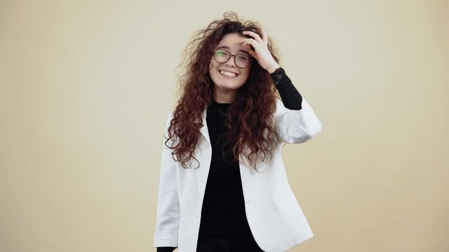 The enthusiastic young woman with curly hair shows her gesture well with her hand and winks. Young hipster in gray jacket and white shirt,