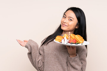 Teenager Asian girl holding waffles isolated on beige background