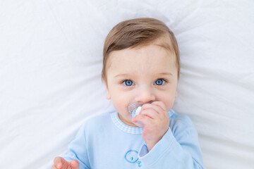 baby boy with pacifier on bed before going to bed in blue bodysuit, happy healthy little baby