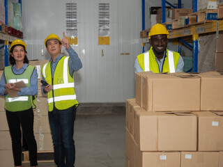 A team of warehouse workers is standing to inspect the finished goods for delivery to customers in the preparation area for delivery within the warehouse.