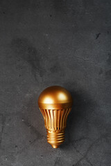 Gold light bulb on a black textured background.