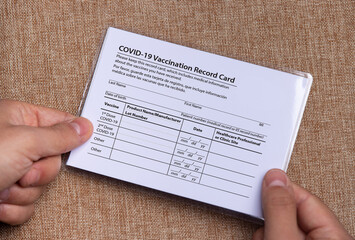 The laminated coronavirus vaccination card is held in the hands. The concept of defeating Covid-19...