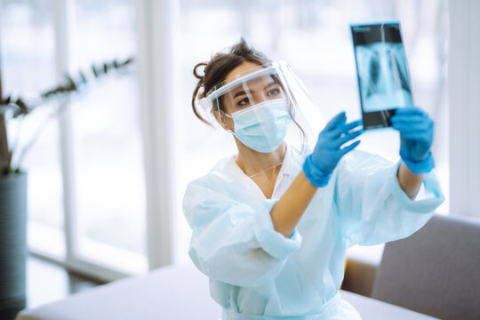 Young Nurse In Visor And Protective Gloves Examines An X-ray  Lung. Pneumonia.X-rays Of Light. Fluorography. Covid-2019.