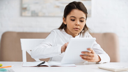 Girl using digital tablet near notebook and blurred calculator.