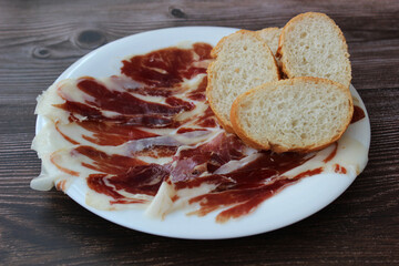 Iberian ham with slices of white bread on wooden background