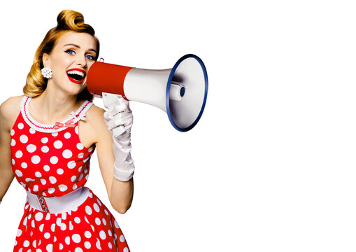 Beauty blond haired woman holding megaphone, shout something. Girl in red pin up style dress in polka dot, isolated over white background. Caucasian model in retro and vintage studio concept.