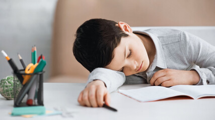 Preteen boy lying near notebook and stationery on table.