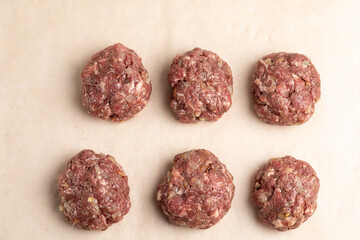 The process of making meatballs from beef meat. Six unroasted raw meat balls laid out on baking paper. View from above.