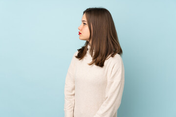 Teenager girl isolated on blue background looking side