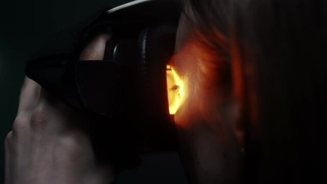 Close-up: A girl puts a virtual reality headset over her eyes. Looks inside the glass of augmented reality glasses. Neon light in the studio. Digital entertainment and arts, immersion