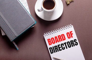 On a brown background, diaries, a white cup of coffee and a notebook with BOARD OF DIRECTORS