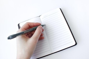  Woman hand is writing on a notebook with a pen on white background. Top view