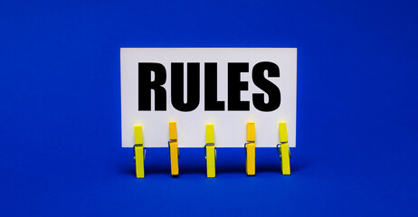 On a bright blue background on yellow clothespins, a white card with the text RULES