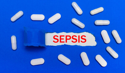 White pills lie on a beautiful blue background. In the center is white paper with the inscription SEPSIS. Medical concept. View from above.