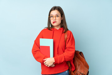 Student girl holding books isolated on blue background having doubts and with confuse face expression