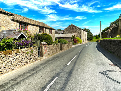 View along, Bracewell Lane, with dry stone walls, a graveyard, and hills in the distance in, Bracewell, Barnoldswick, UK