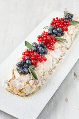 Meringue dessert Pavlova cake with fresh berries on top on a light wooden background.