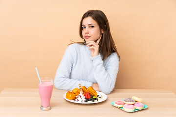 Obraz na płótnie Canvas Teenager girl eating waffles isolated on beige background thinking