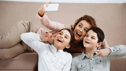 Cheerful family showing peace sign while taking selfie on couch.