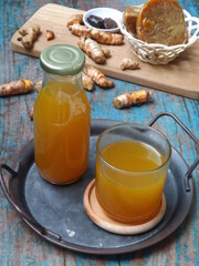 Jamu kunir asem or kunyit asam is Indonesian traditional herbal drink made from turmeric, tamarind, palm sugar. Served on tray with ingredients as background. Better served cold. Healthy refreshment.