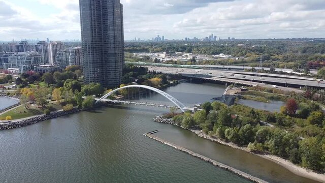 Aerial lateral flight looking at a passenger train speed by next to the Gardiner Expressway with the Humber Bay bridge and water in the foreground