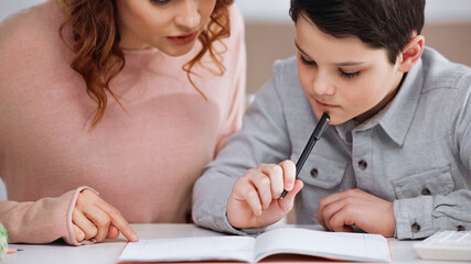 Mother sitting near child with pen doing homework.