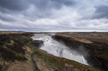 Fototapeta na wymiar Famous Gulfoss waterfall in the Golden Circle in South Iceland. Unrecognizable tourists walk on a path to the viewpoint. Wide landscape view
