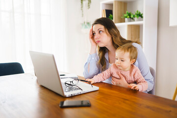 sad and frustrated mother in kitchen home office with computer and her daugher