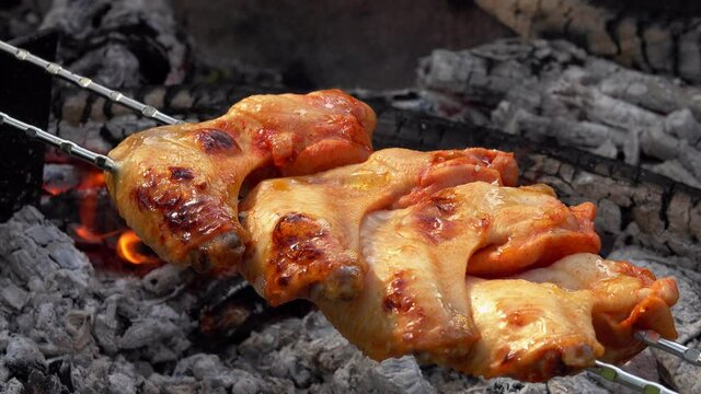 Delicious marinated chicken wings on the skewers are frying above the open fire in a rapid footage