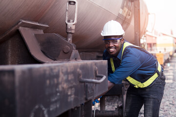 African machine engineer technician wearing a helmet, groves and safety vest is using a wrench to repair the train transport gas and oil